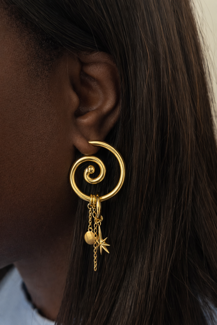 Gold spiral earring with dangling charms worn by a person